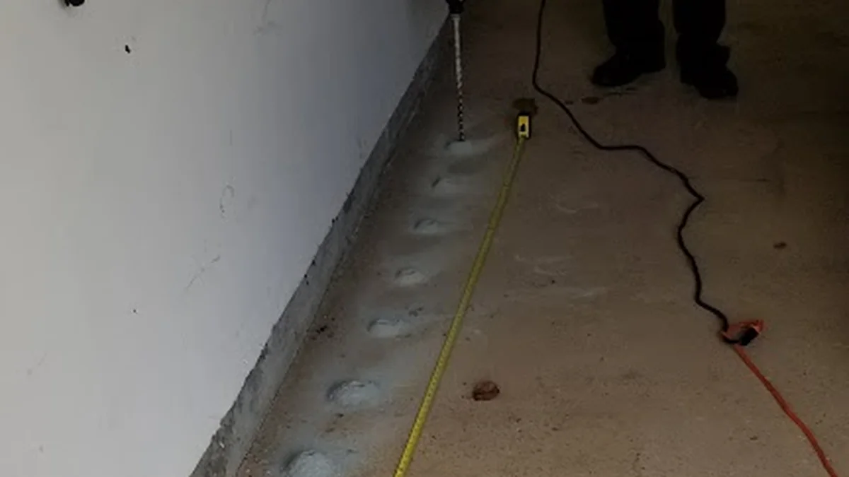 Technician installing an in-ground termite monitoring station by a foundation