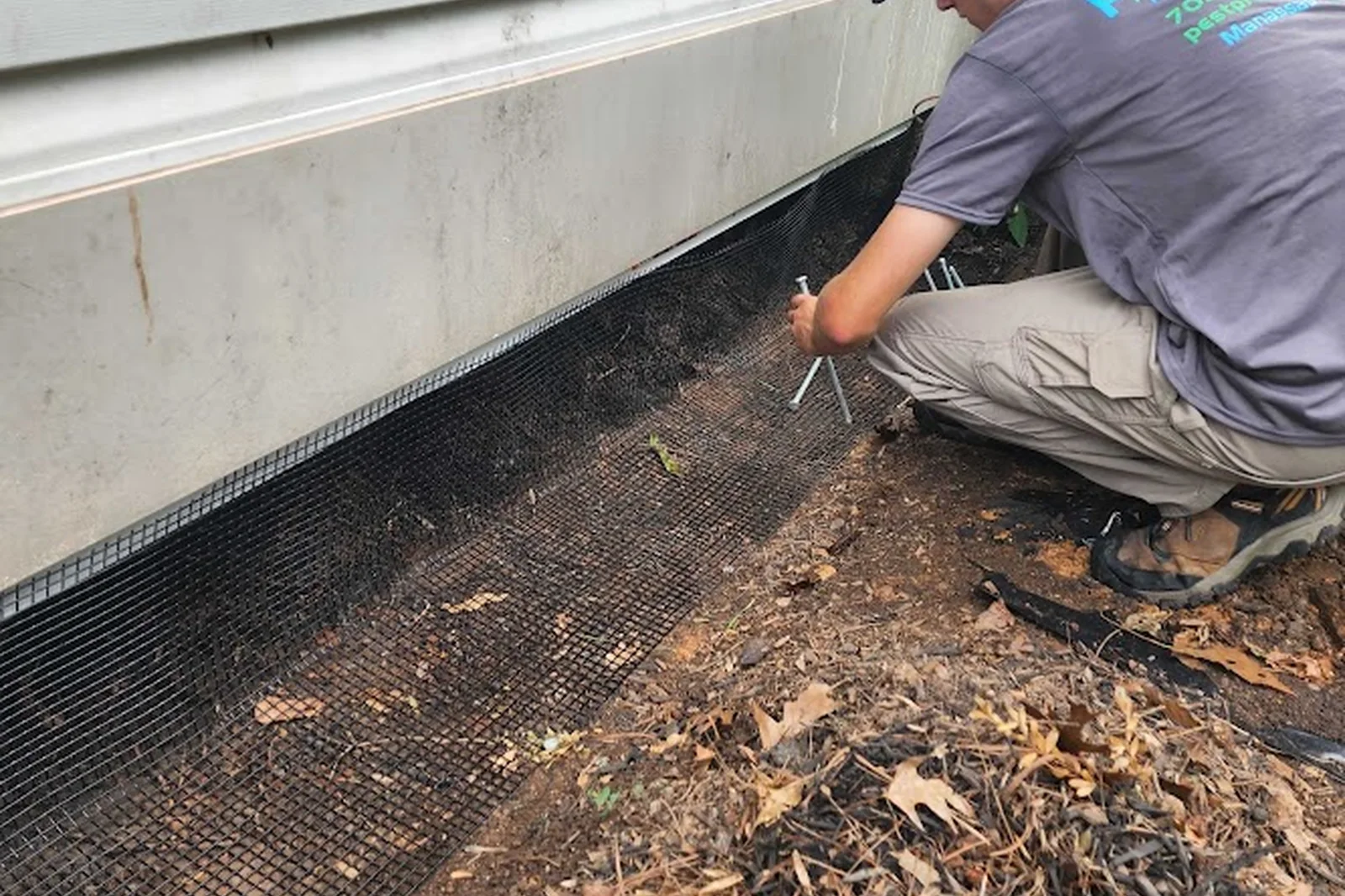 Pest Proof technician in protective coverall installing exclusion mesh in a crawl space